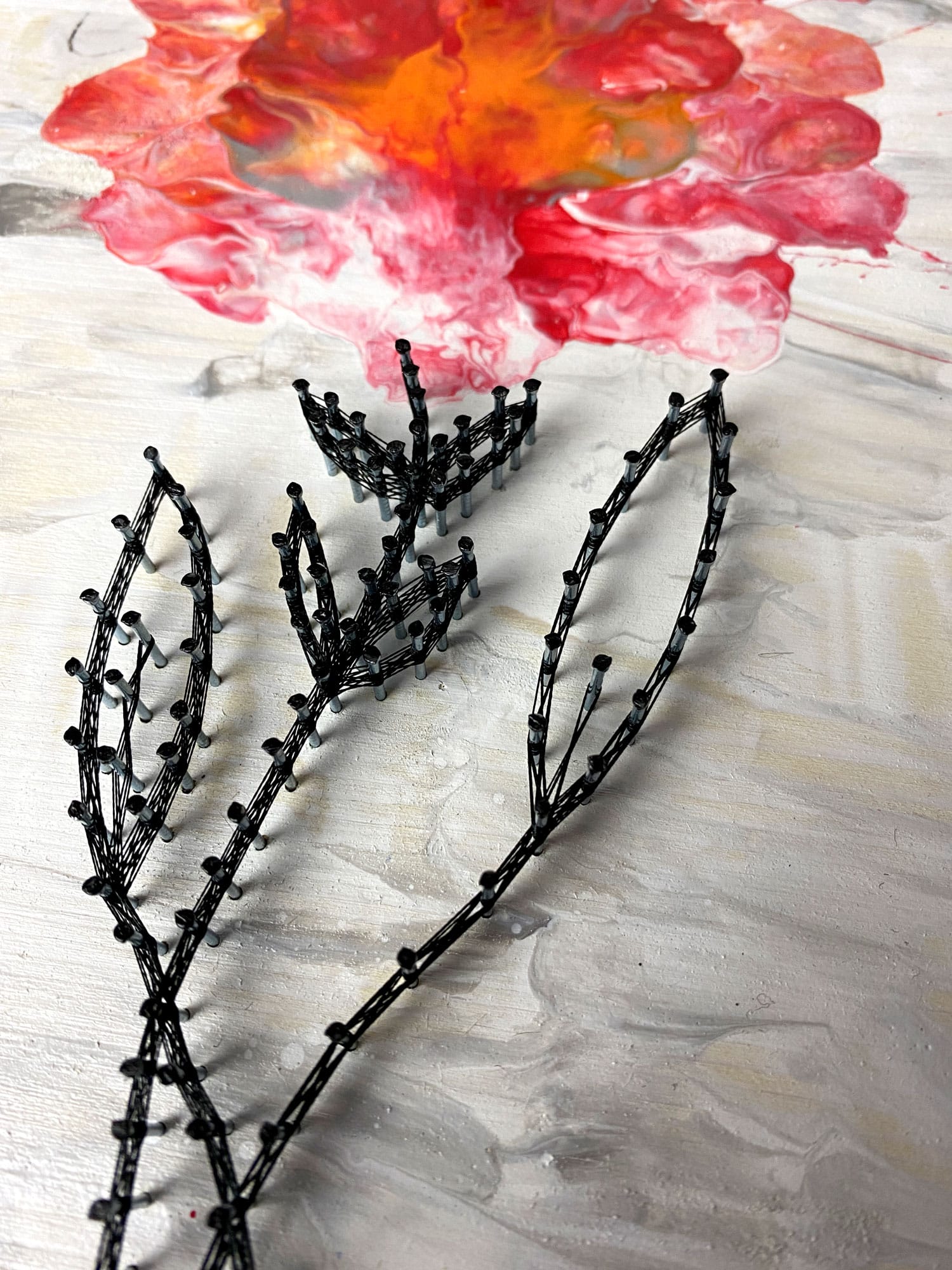 Fadenbild mit Acrylic Pouring als Blume im Detail das Garn.