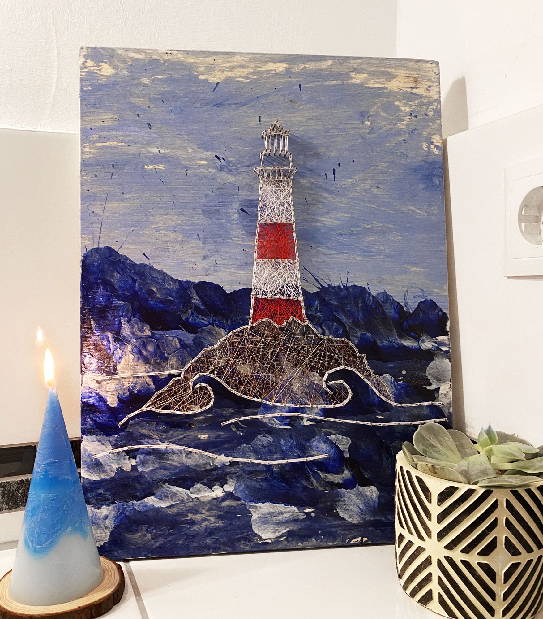 An Wand anlehnendes Leuchtturm Fadenbild mit Blume und Kerze als Deko