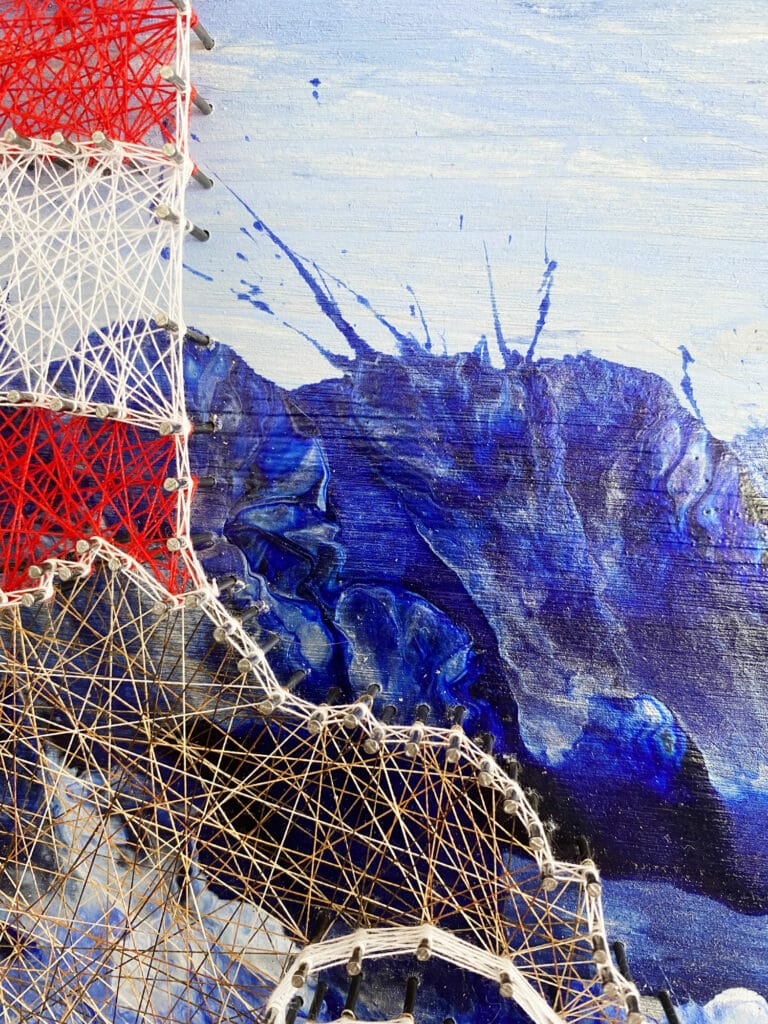 Nachaufnahme des Fadenbildes Leuchtturm mit abstrakten Wellen vom Acrylic Pouring im Hintergrund