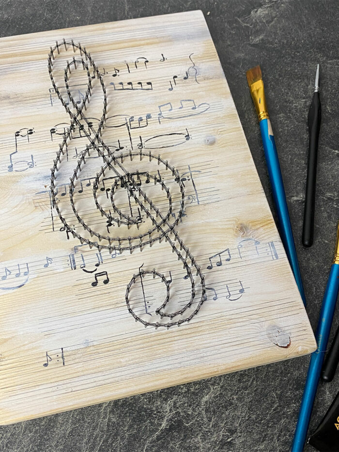 Fadenbild mit Violinschlüssel und gemalten Noten im Hintergrund